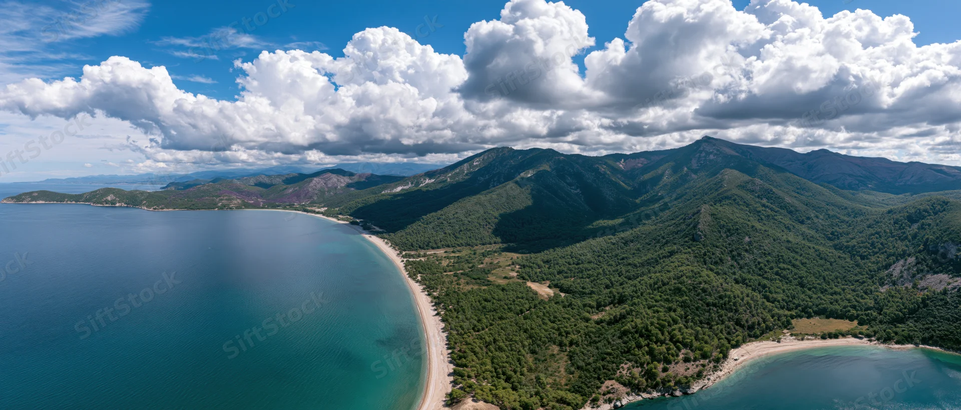 Aerial view of a coastal landscape with mountains, forest, and sandy beaches along the sea