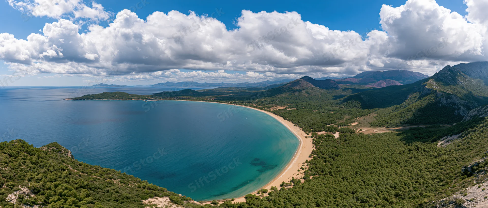 Curved sandy beach nestled between green hills and turquoise sea under a bright blue sky with white clouds