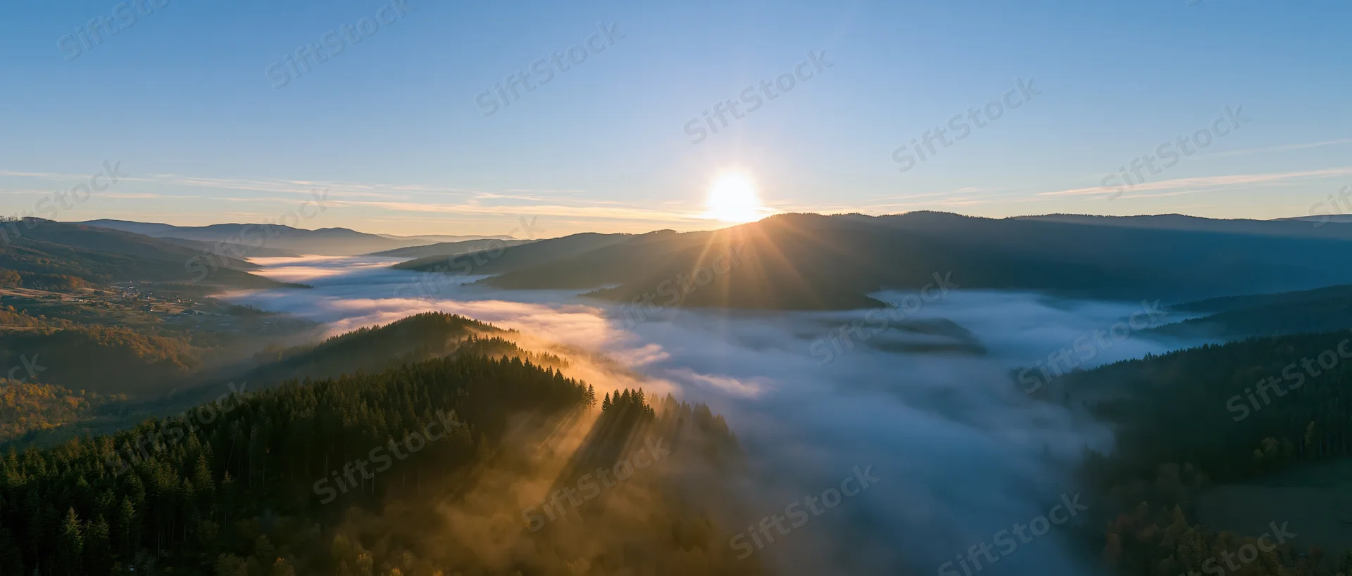 Sunrise over misty mountain valley with forested hills and fog-filled lowlands