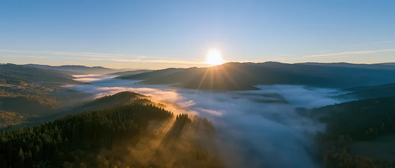 Sunrise over misty mountain valley with forested hills and fog-filled lowlands
