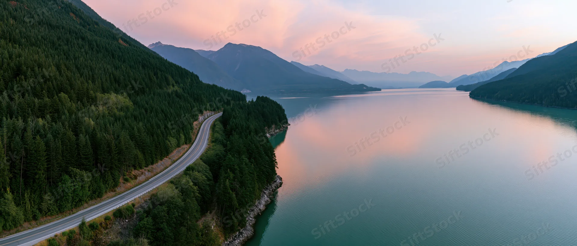 Winding road along a mountain lake at sunset surrounded by dense forest