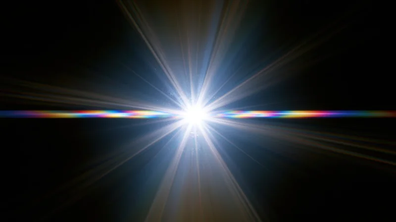 Bright starburst light flare with radial beams and horizontal rainbow spectrum against black background