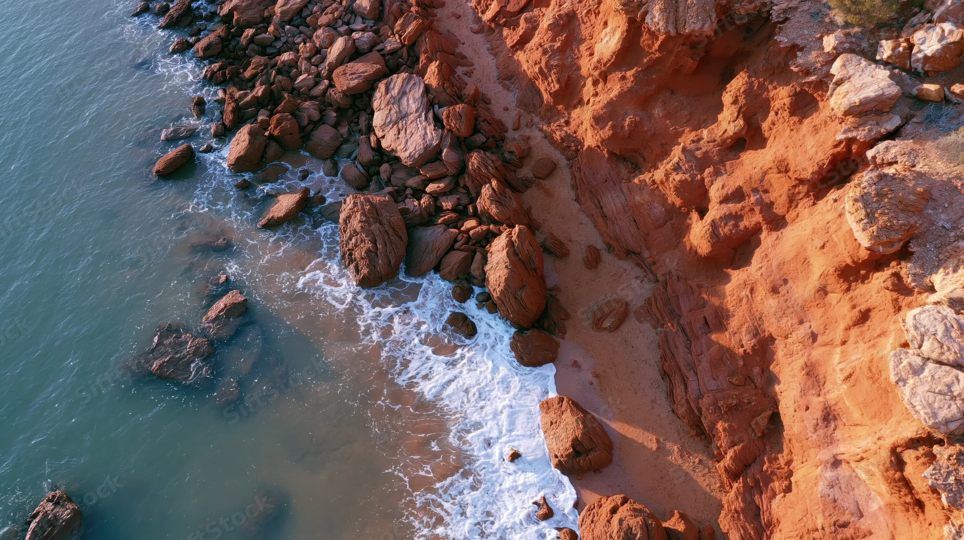 Red rock cliffs meeting ocean waves along rugged coastline