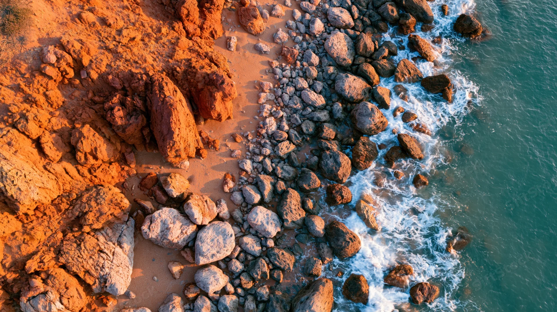 Aerial view of rocky coastline with waves crashing against orange cliffs and sandy beach