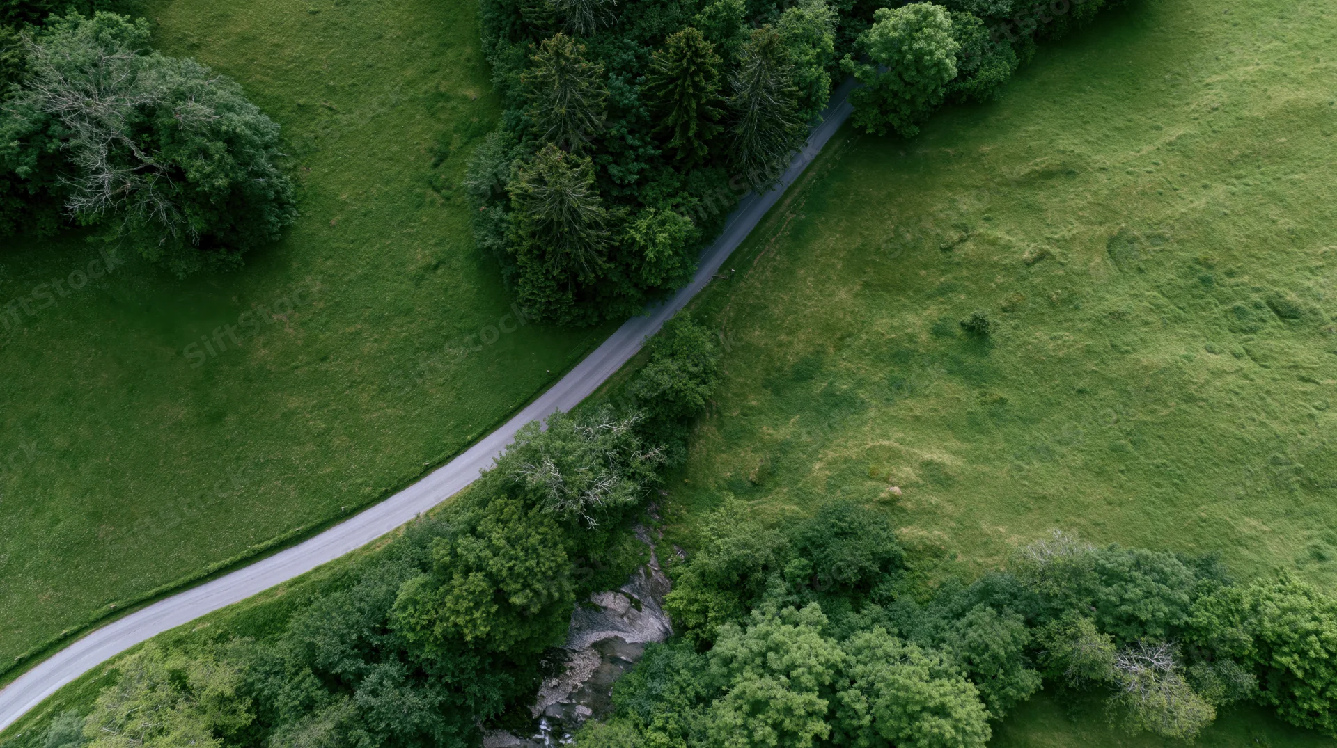 Aerial view of a winding road through green meadows and forested areas