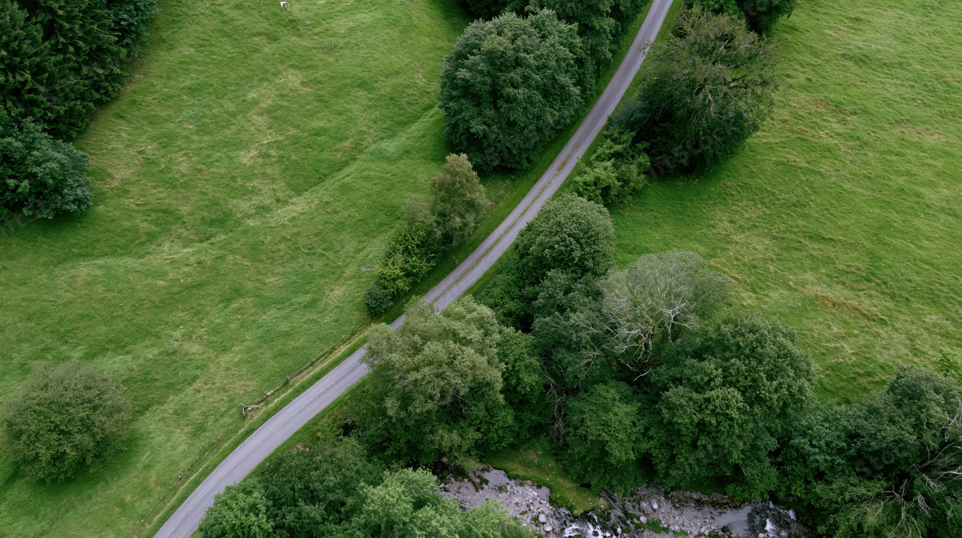 Aerial view of a winding road through green countryside with trees and a stream
