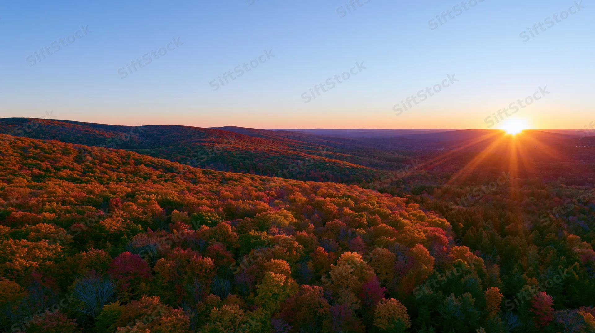 Autumn forest at sunset viewed from above with sun rising over distant hills