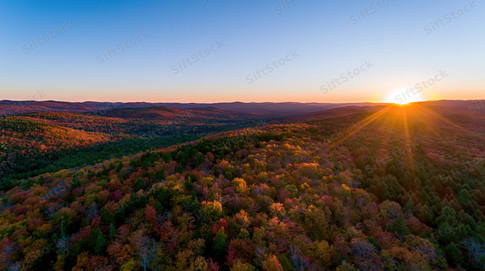 Autumn forest at sunset viewed from above with sun rising over distant hills