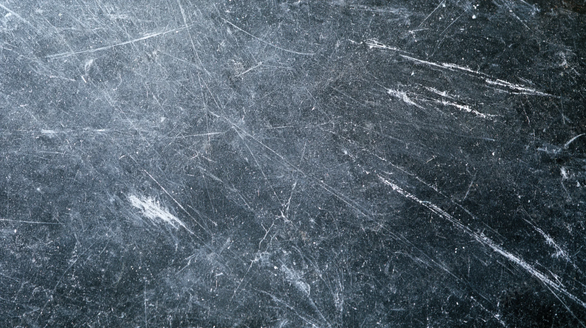Scratched dark metallic surface with white wear marks and scuffs across the frame