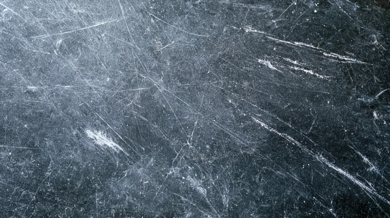 Scratched dark metallic surface with white wear marks and scuffs across the frame
