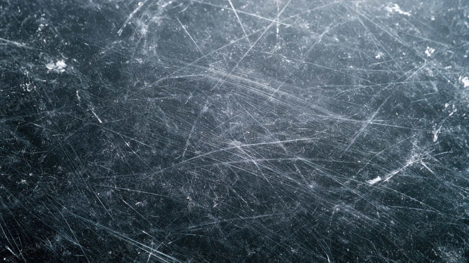 Close-up of scratched dark metallic surface showing network of fine cuts and wear marks