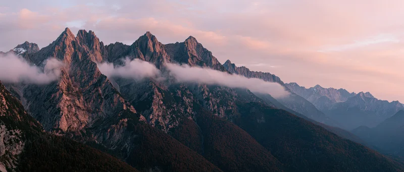 Rugged mountain peaks rising above clouds at sunset with forested slopes below
