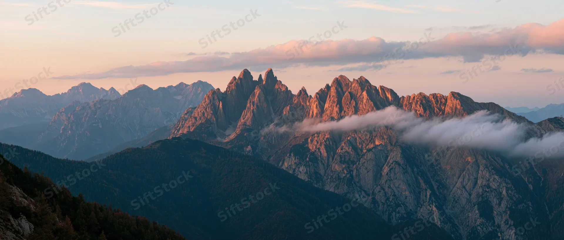 Jagged mountain peaks bathed in golden light at sunset with clouds drifting through the valleys below