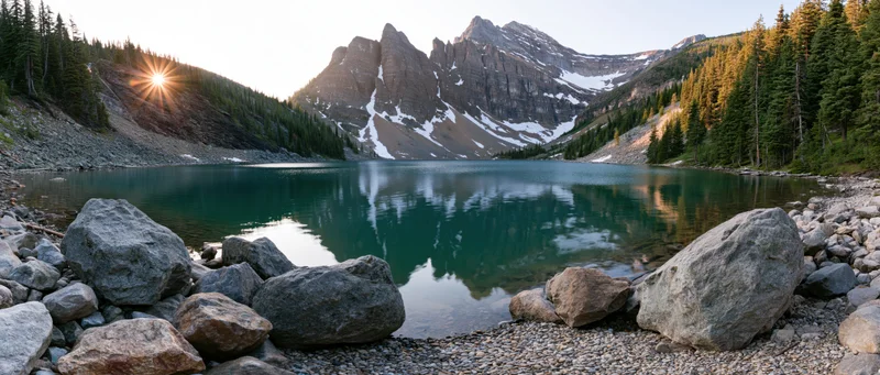 Mountain lake reflecting peaks at sunrise surrounded by pine forest and boulders