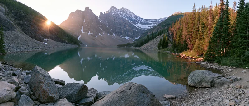 Mountain peaks reflected in calm alpine lake surrounded by evergreen forest at sunrise