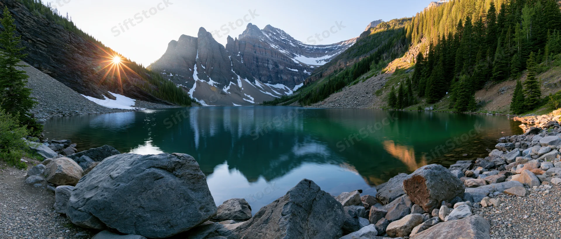 Alpine lake reflecting snow-capped mountains at sunrise surrounded by evergreen forest and rocky shore