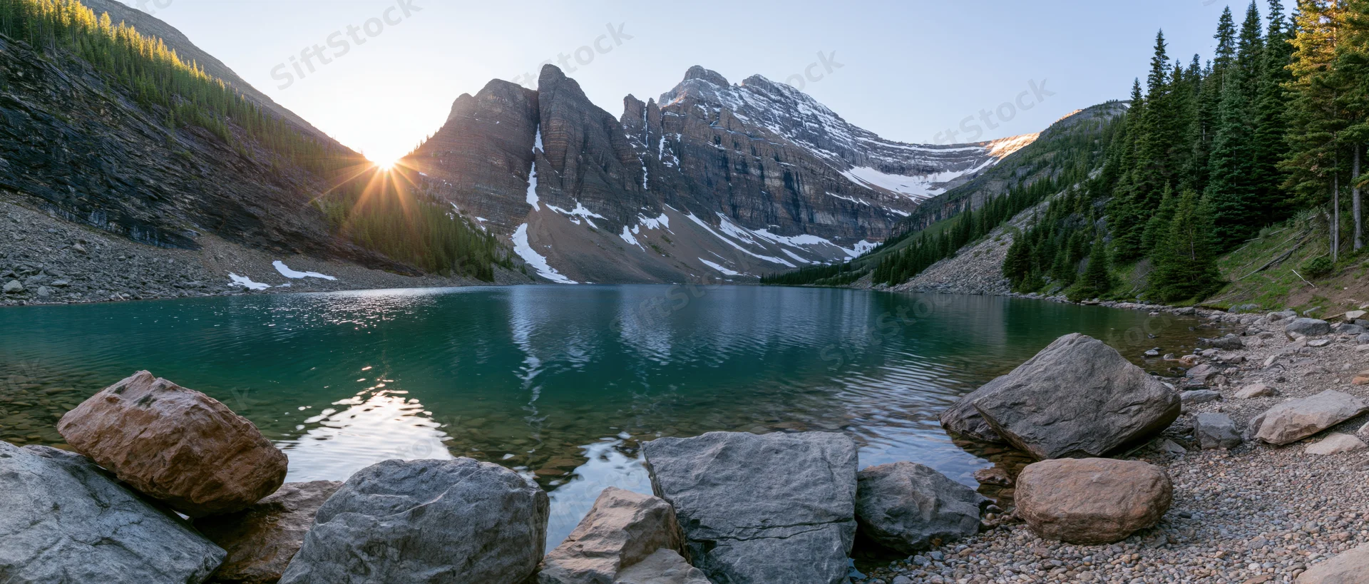 Alpine lake reflecting snow-capped mountains at sunrise surrounded by pine forest and rocky shore