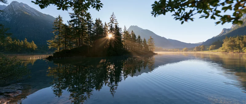Sunrise over a calm lake reflecting pine trees and mountains in an alpine valley