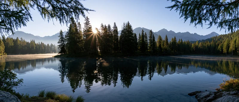 Calm lake reflecting pine trees and mountains at sunrise in alpine forest