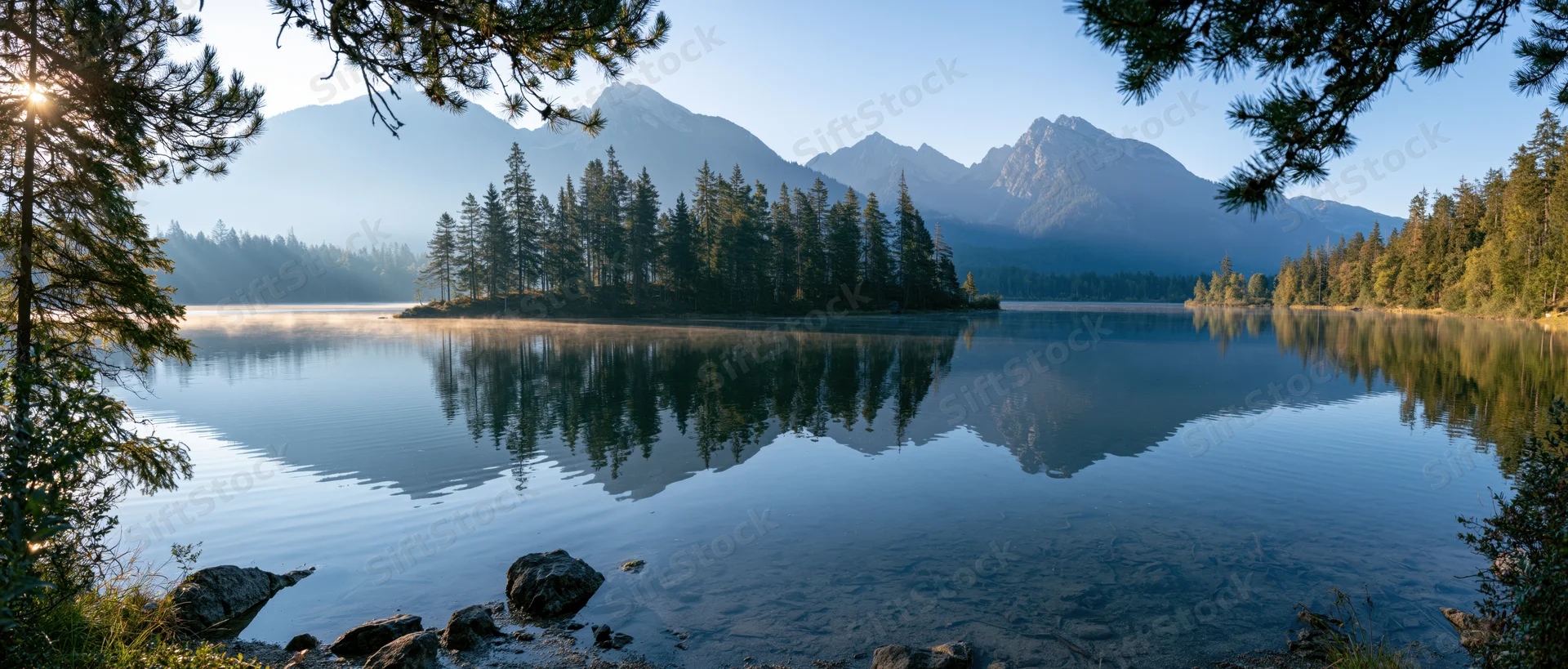 Calm lake reflecting mountains and pine trees at sunrise in alpine wilderness