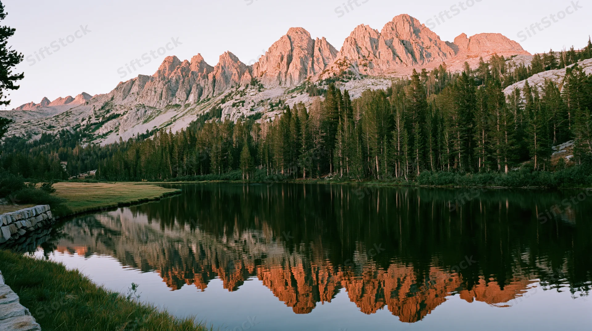 Rocky mountain peaks reflected in calm lake surrounded by pine forest at sunset