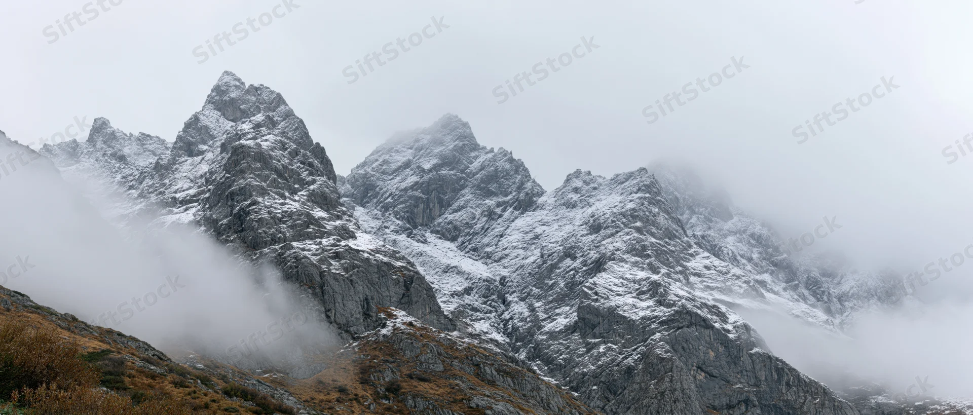 Snow-covered mountain peaks rising above misty clouds in alpine terrain