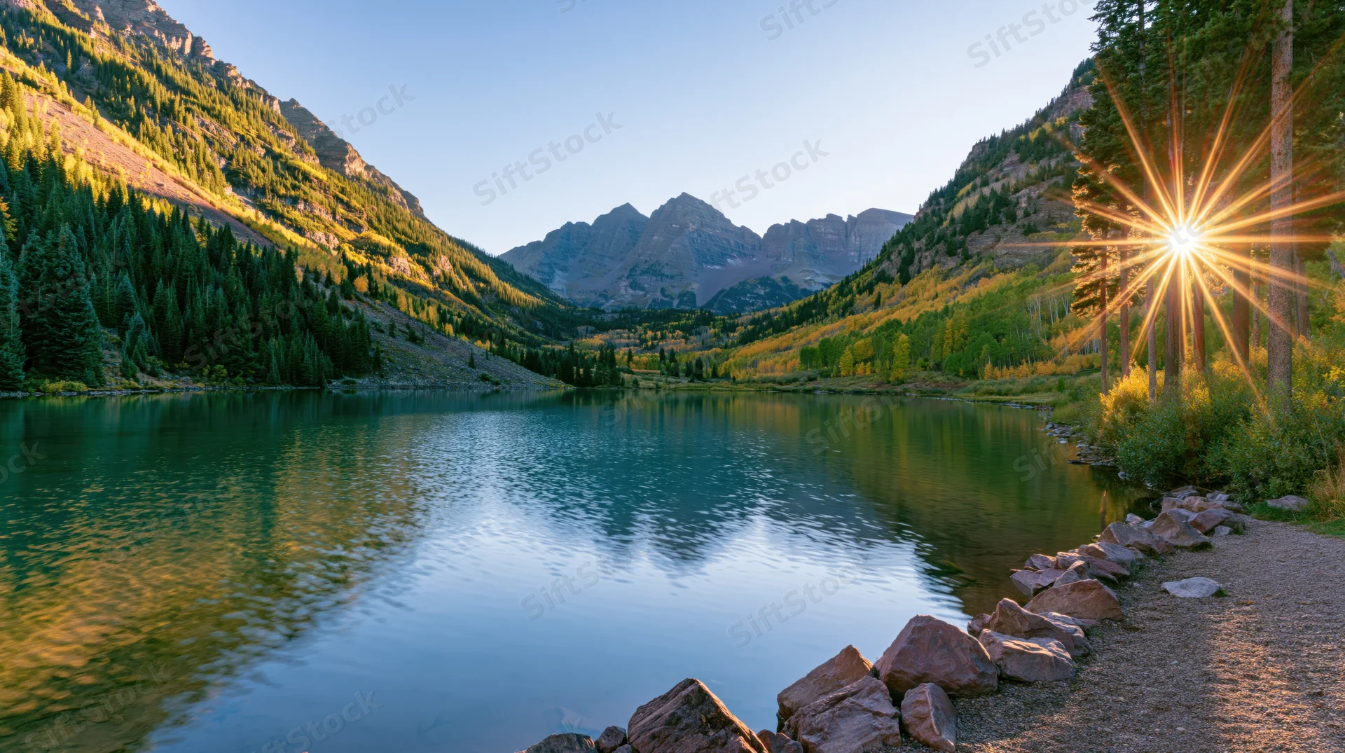 Calm lake reflecting mountains and trees at sunrise in alpine valley
