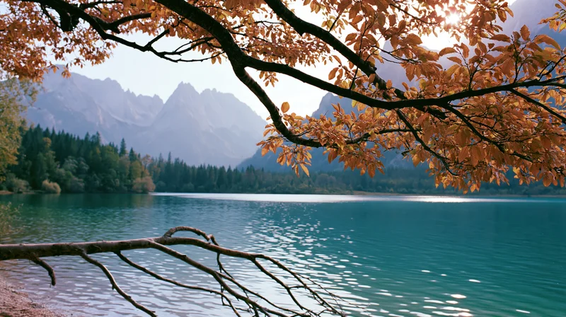 Autumn tree branches framing a calm lake with mountains in the background