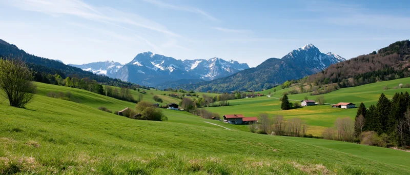 Green alpine valley with scattered farmhouses and snow-capped mountains in the distance