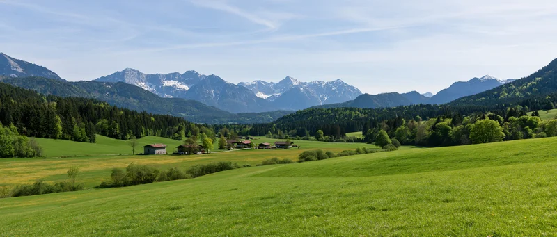Green meadow with farmhouses and snow-capped mountains in the alpine valley