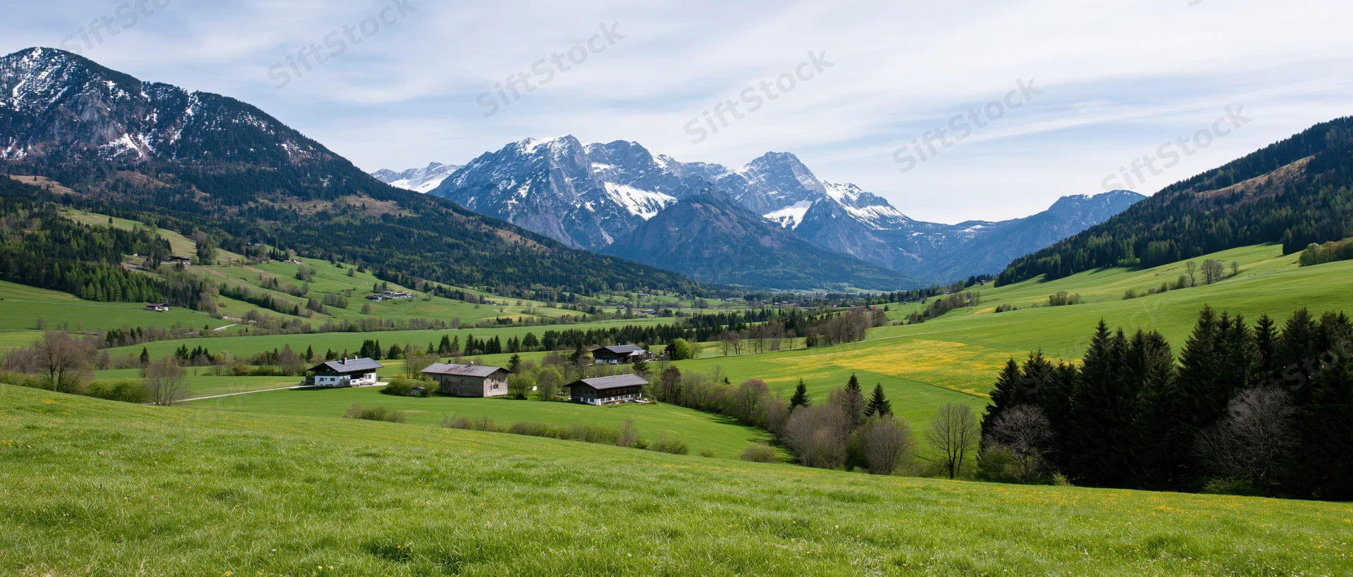 Alpine valley with green meadows and farmhouses nestled among snow-capped mountains