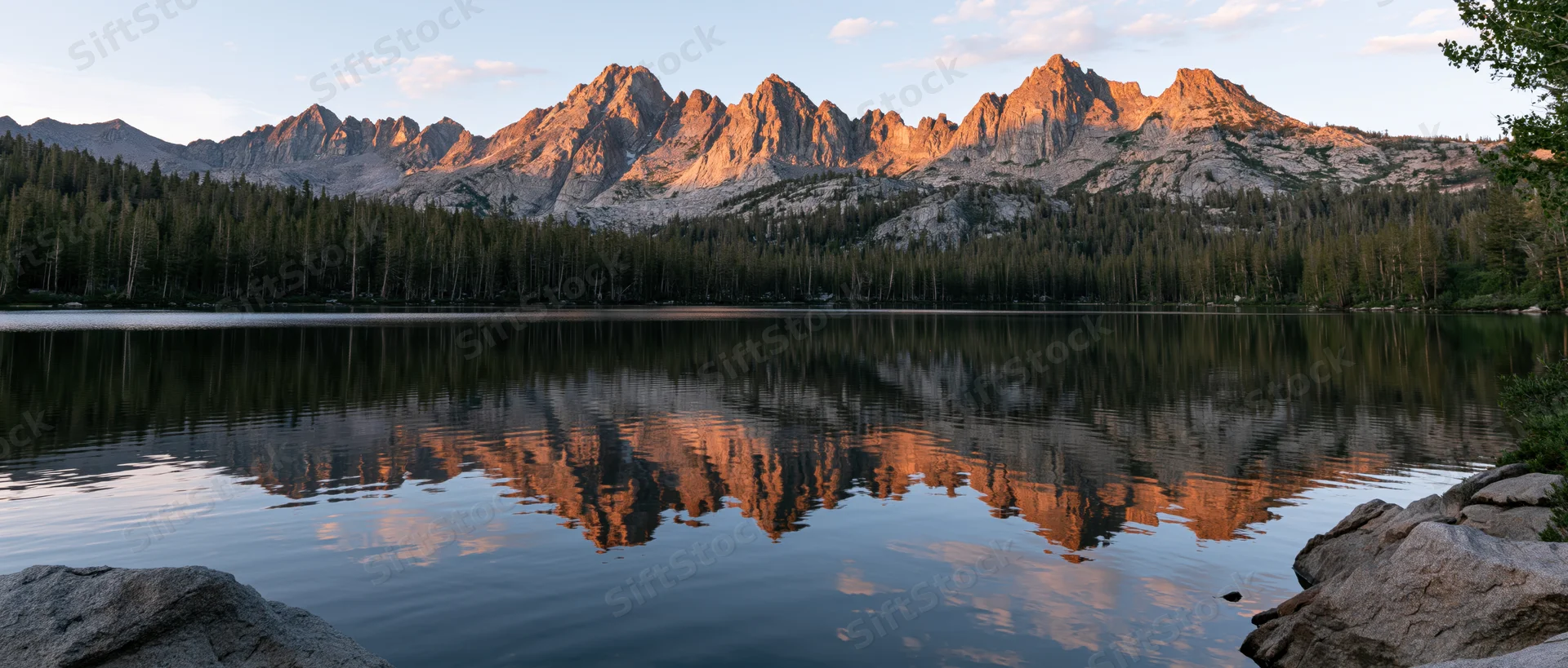 Rugged mountain peaks reflected in calm lake waters at sunset surrounded by dense evergreen forest