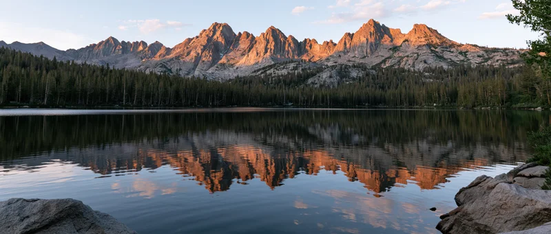Rugged mountain peaks reflected in calm lake waters at sunset surrounded by dense evergreen forest