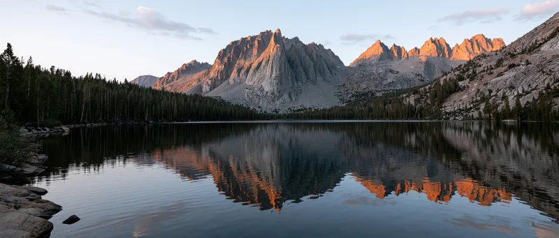 Rugged granite mountains reflected in a calm alpine lake at sunset surrounded by evergreen forest