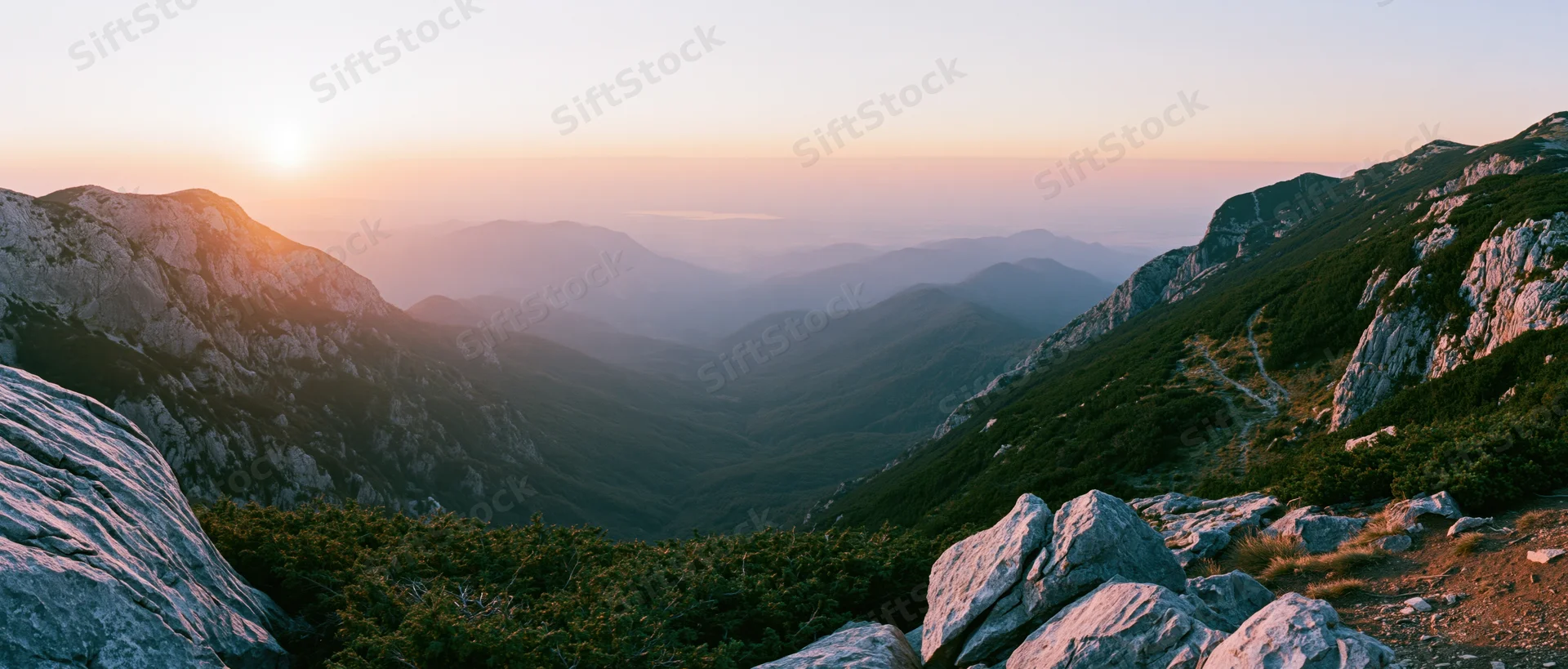 Sunrise over a mountain valley with rocky ridges and distant peaks in the distance