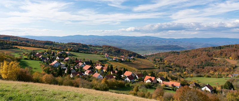 Village nestled among autumn-colored hills and fields under a blue sky with scattered clouds