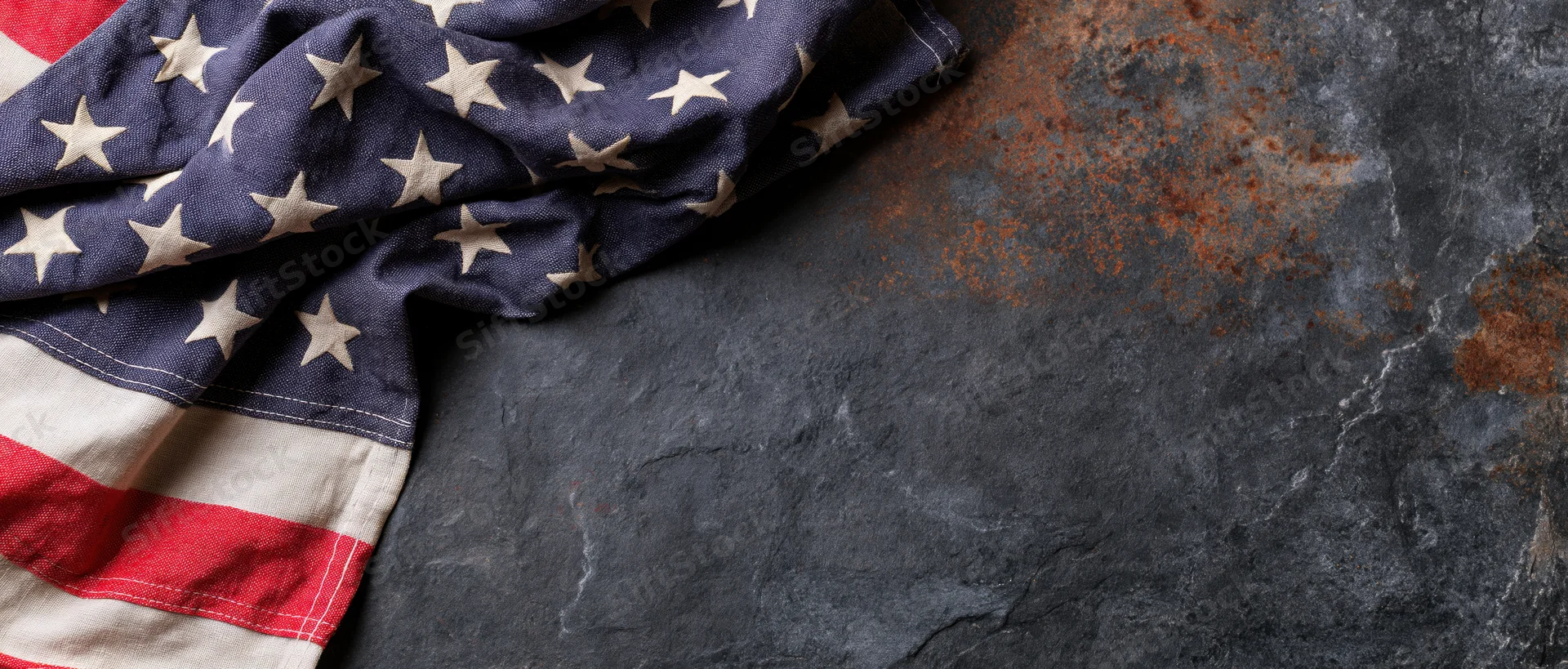 American flag with stars and stripes draped on a dark textured stone surface with rust stains and copyspace