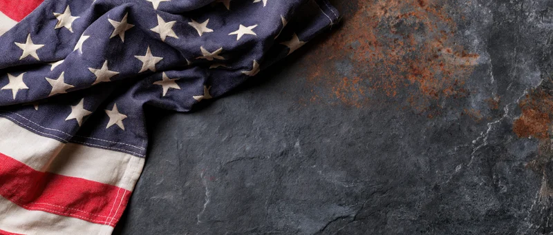 American flag with stars and stripes draped on a dark textured stone surface with rust stains and copyspace