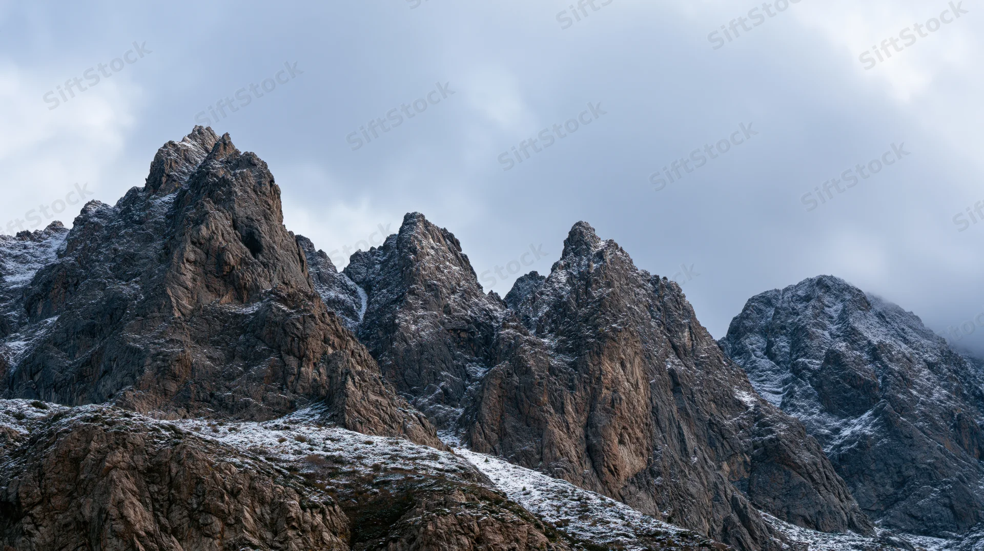 Jagged mountain peaks with snow dusting under overcast sky