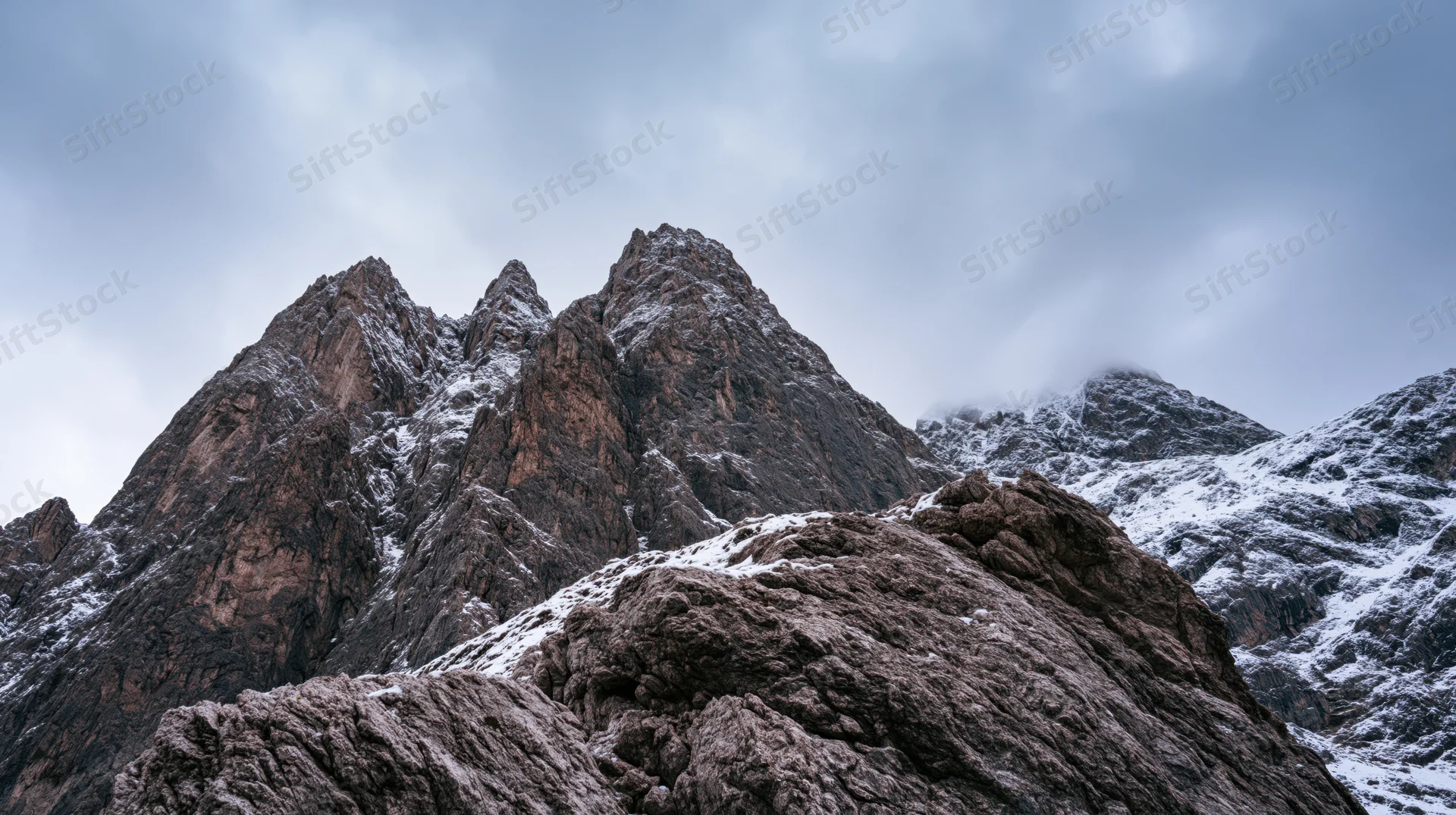 Snow-dusted rocky mountain peaks rising under an overcast sky