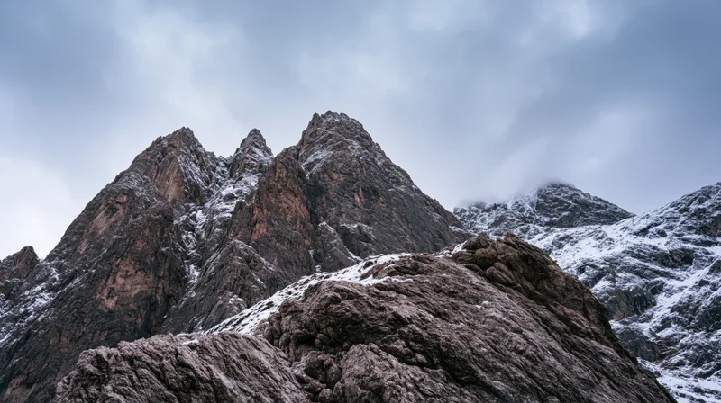 Snow-dusted rocky mountain peaks rising under an overcast sky