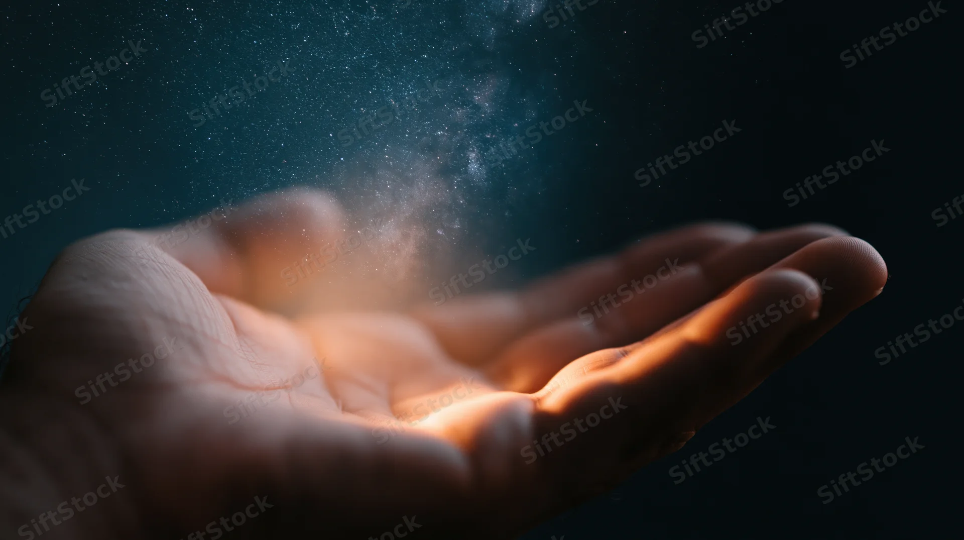 Hand holding glowing cosmic dust against dark night sky