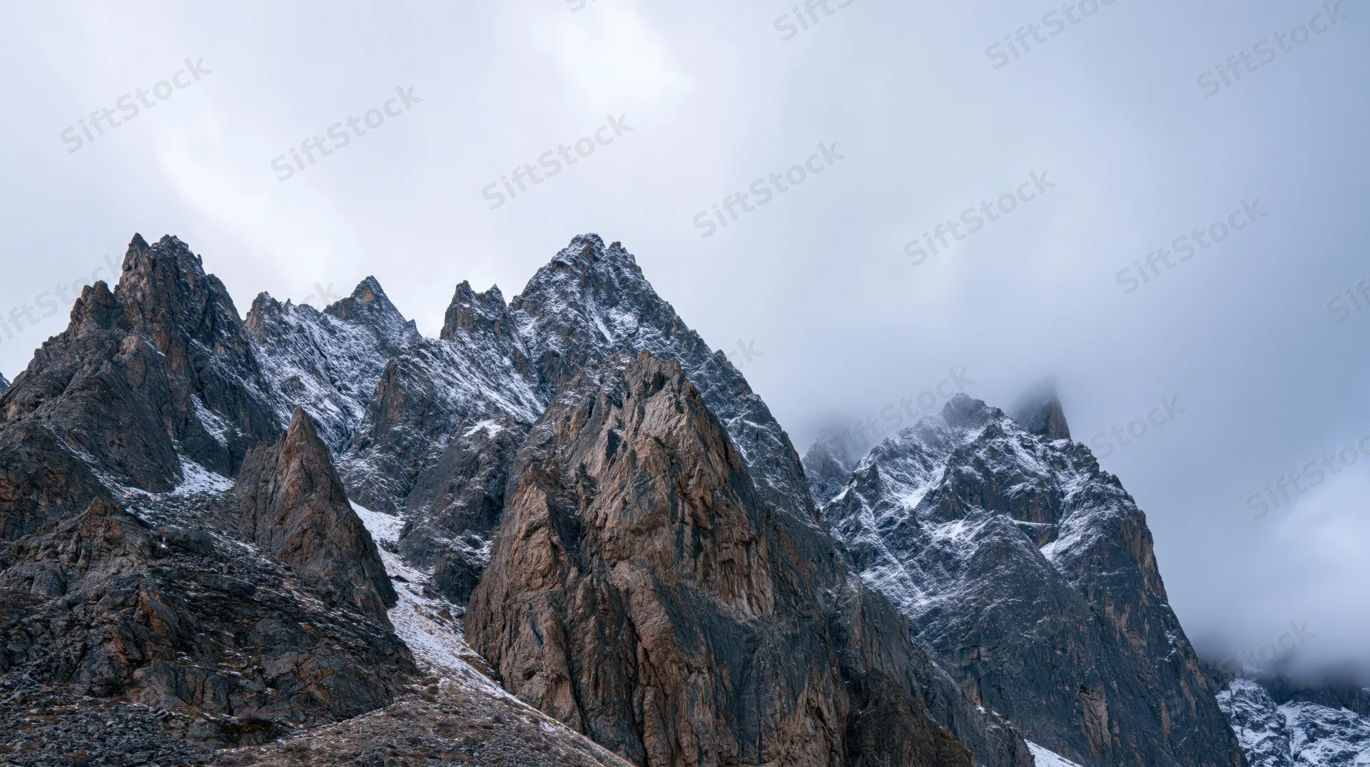 Jagged snow-dusted mountain peaks rising under overcast sky