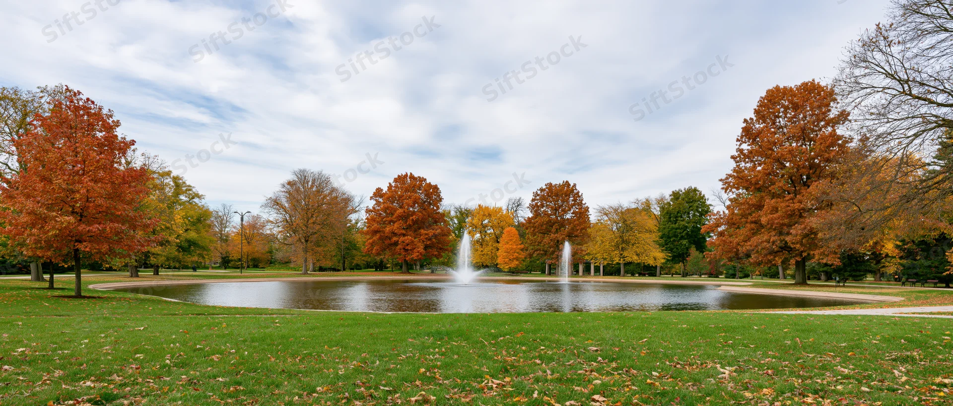 Autumn trees with colorful foliage surrounding a pond with fountains in a city park