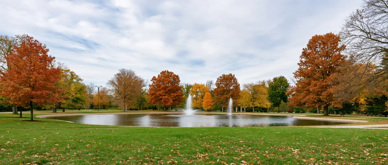 Autumn trees with colorful foliage surrounding a pond with fountains in a city park