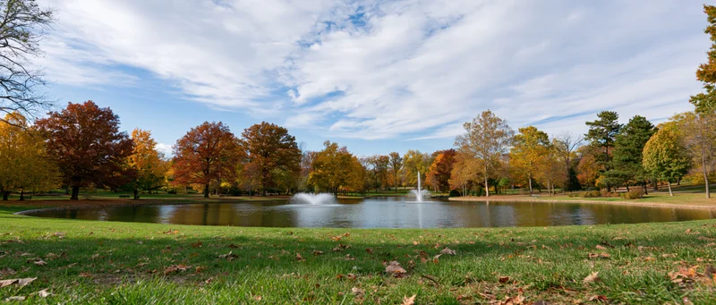 Autumn trees with colorful foliage surrounding a pond with fountain in a park