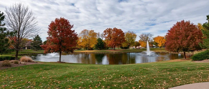 Autumn trees with colorful foliage surrounding a calm pond with fountains in a park setting