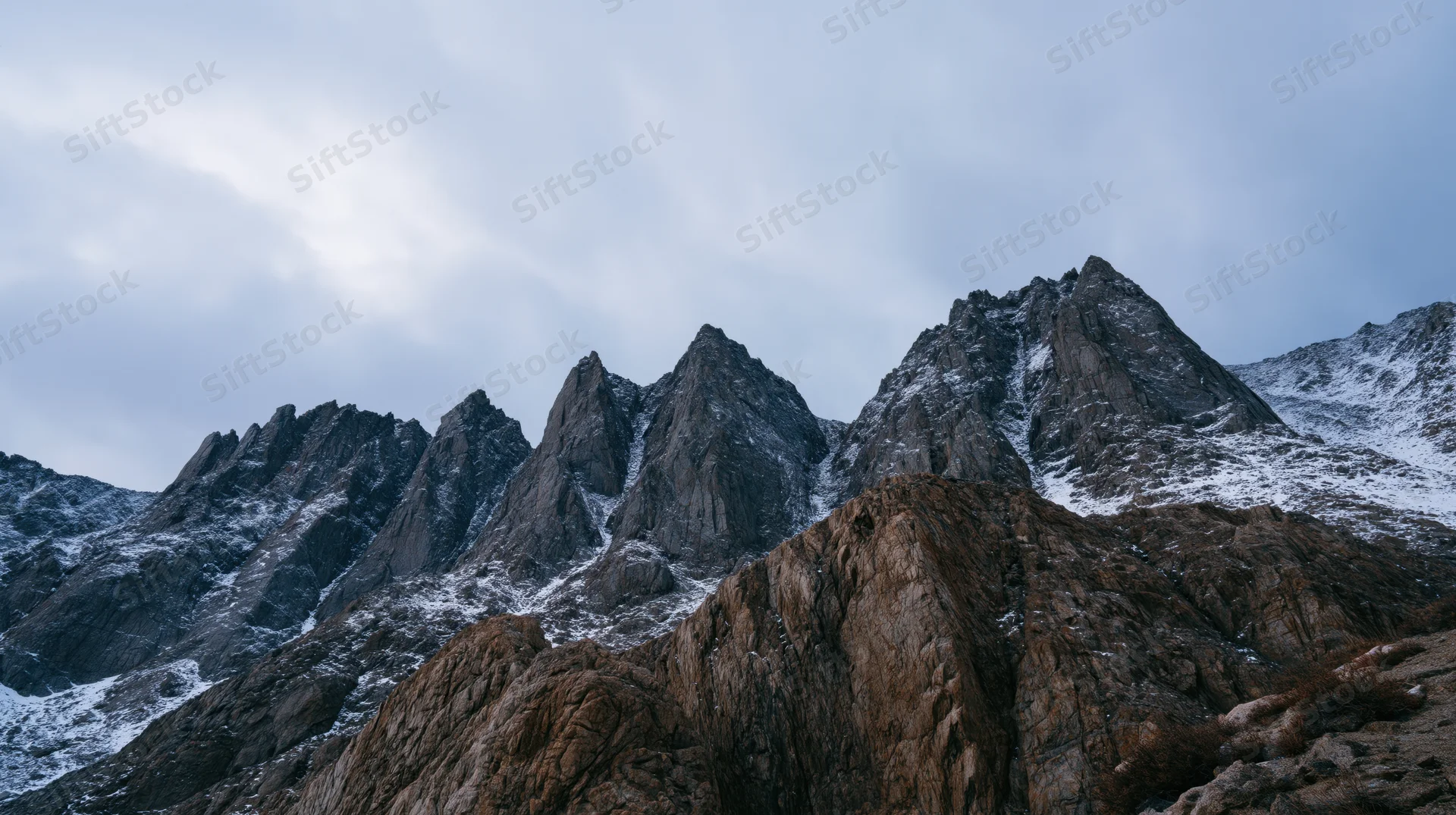 Jagged mountain peaks with snow patches under overcast sky