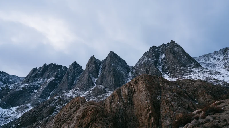 Jagged mountain peaks with snow patches under overcast sky