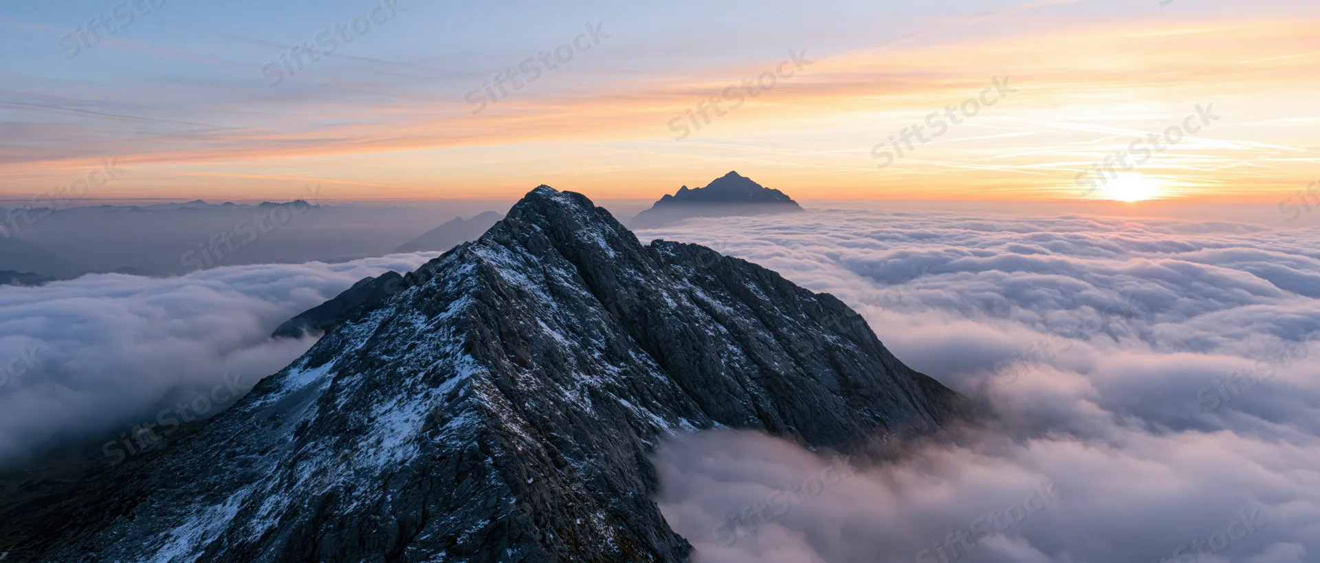 Snow-covered mountain peak rising above a sea of clouds at sunrise